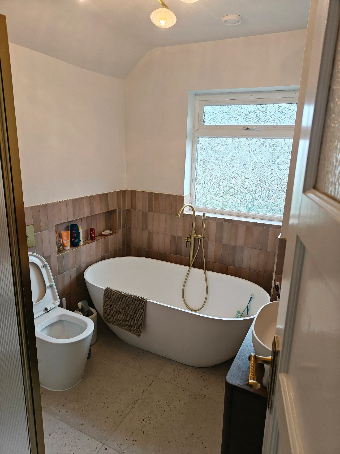 After: the same bathroom renovated with a freestanding tub, terracotta tiles and brass fixtures