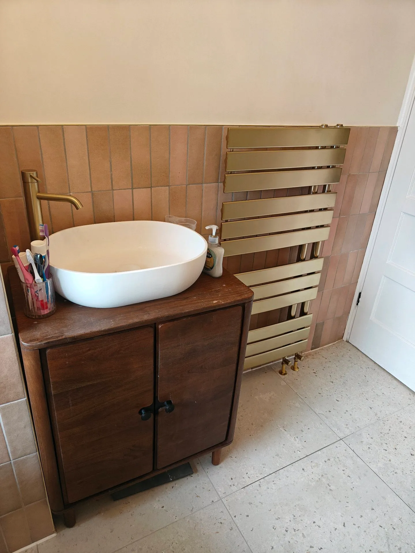 Renovated bathroom detail: wood vanity with countertop basin and brass towel radiator