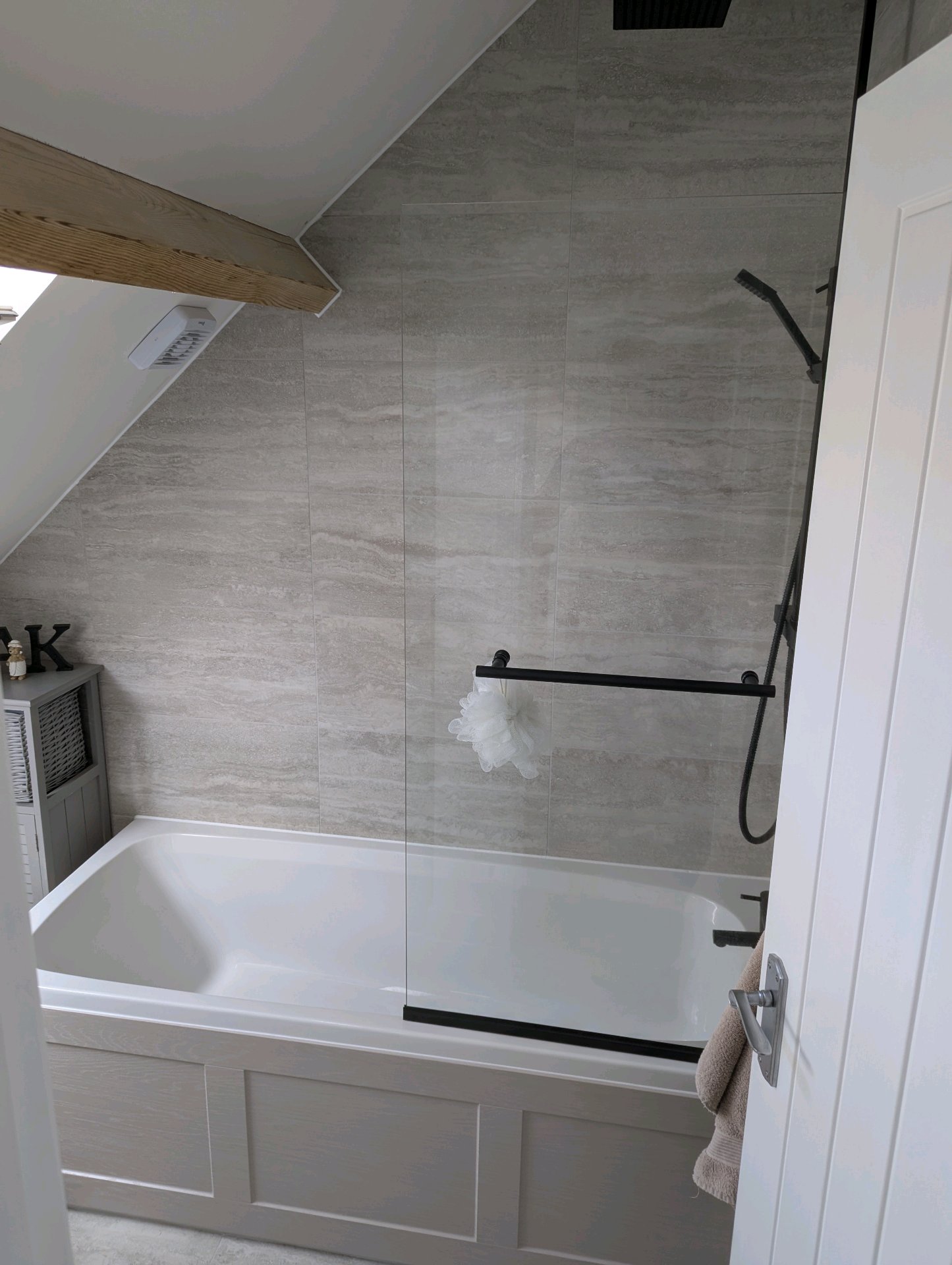 After: Elegant loft bathroom with grey stone-effect tiles, panelled bath, black shower