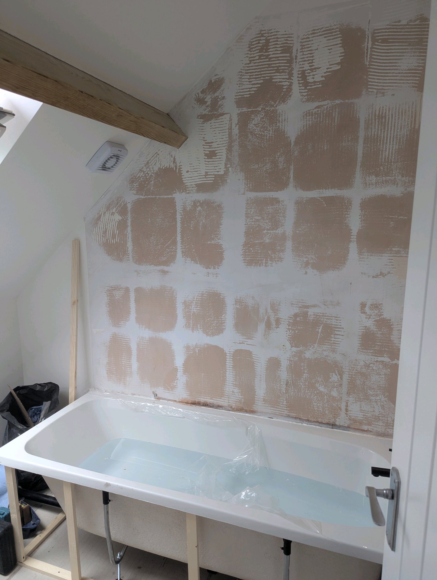 During: Loft bathroom mid-renovation with walls stripped and tile adhesive visible