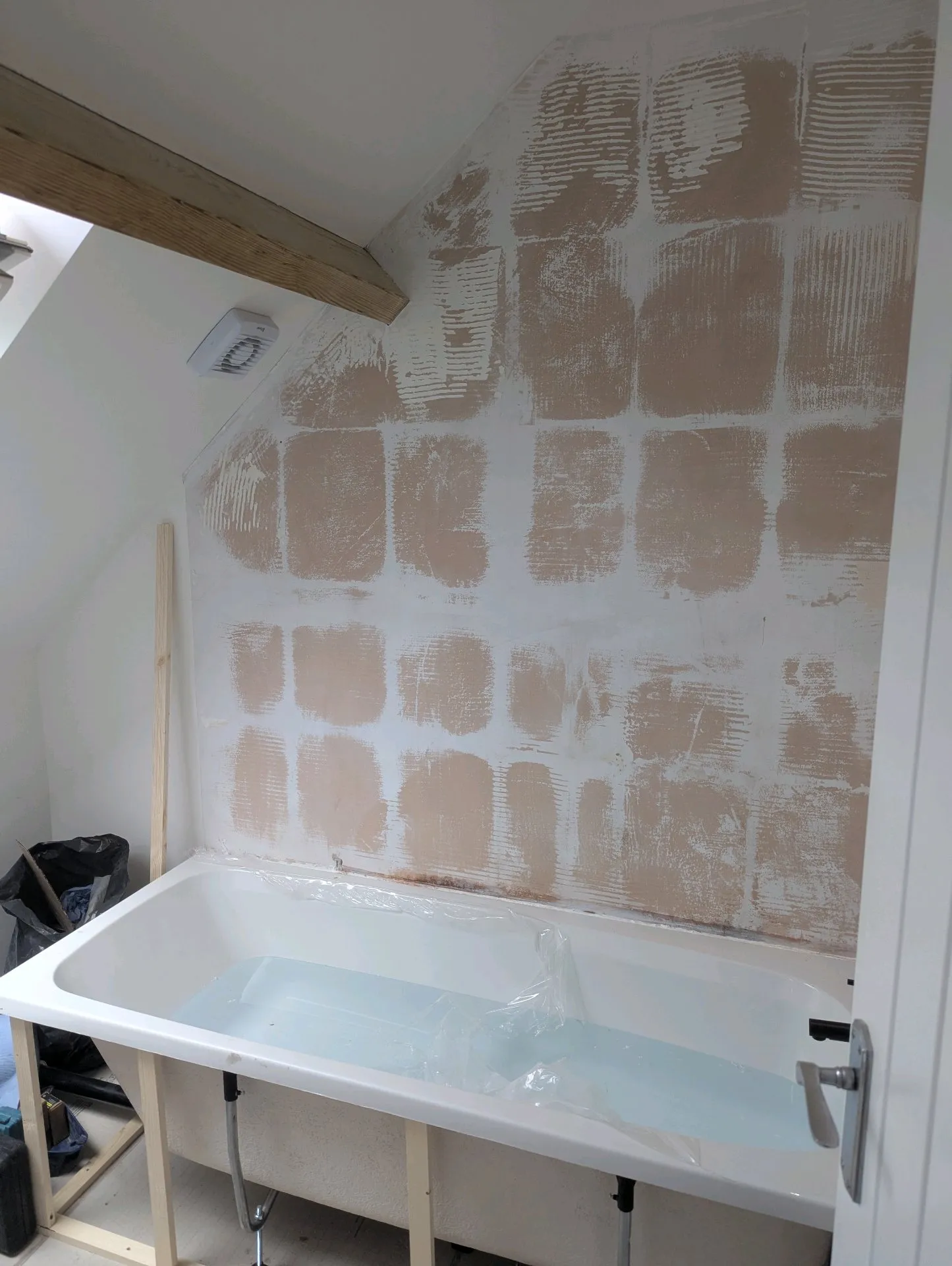 During: Loft bathroom mid-renovation with walls stripped and tile adhesive visible